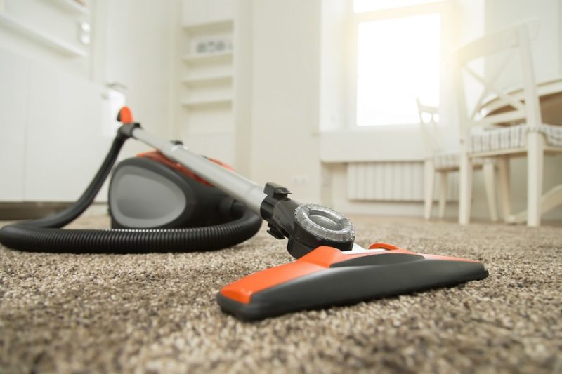 Black and orange vacuum cleaner standing on fluffy carpet in the living room before or after the cleaning. Home, housekeeping concept.